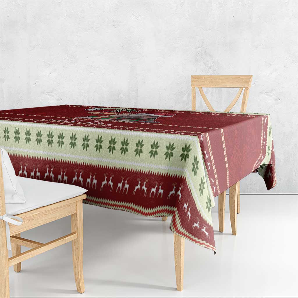 Red holiday tablecloth draped over table with green leaf and Santa figures