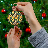 Handheld round ceramic ornament showing a sloth and orange flowers on dark green leaves