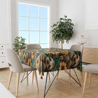 Green tablecloth with sloths and yellow flowers, draped over dining table.