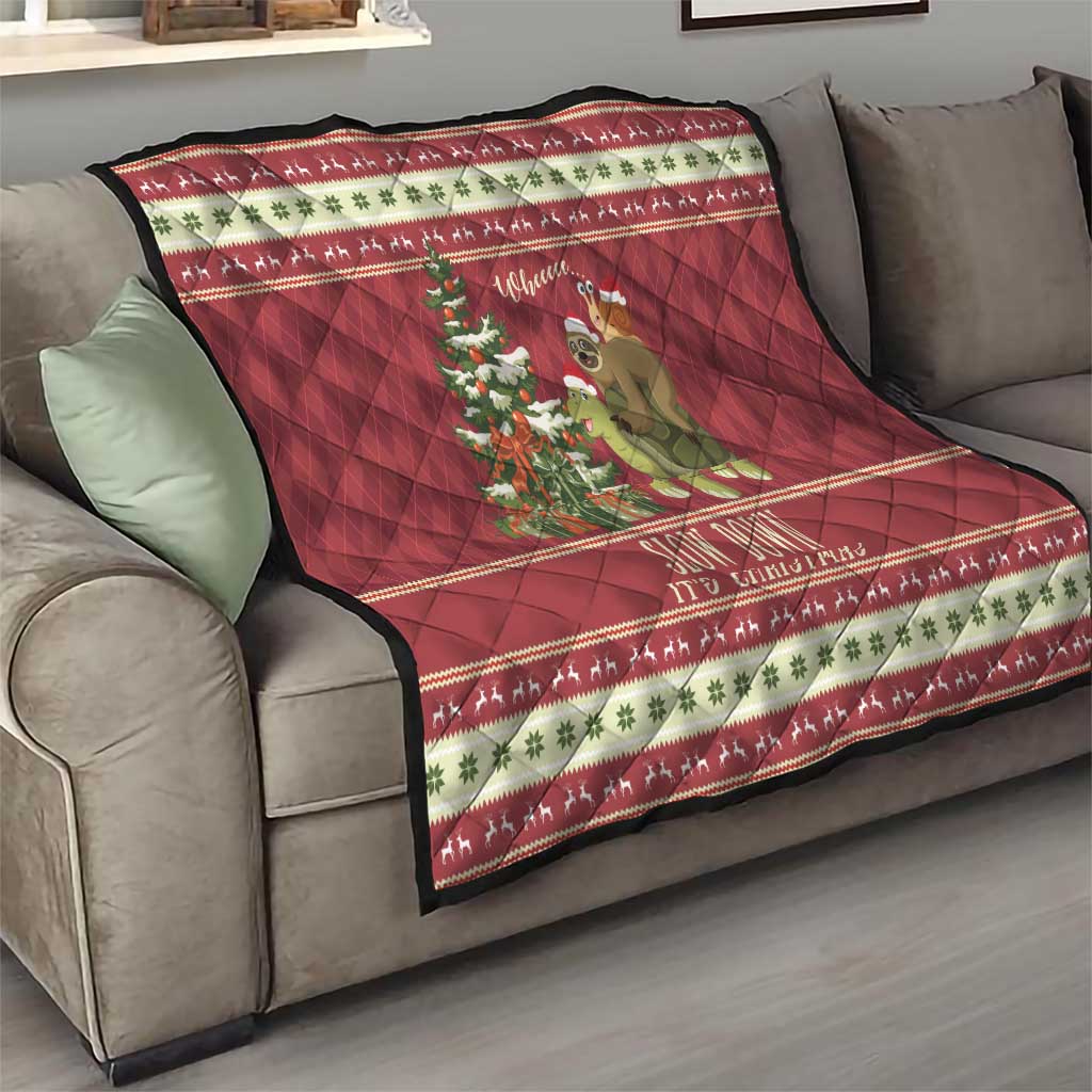 Red Christmas quilt on sofa with central sloth-and-turtle graphic, tree, and festive stripe border.
