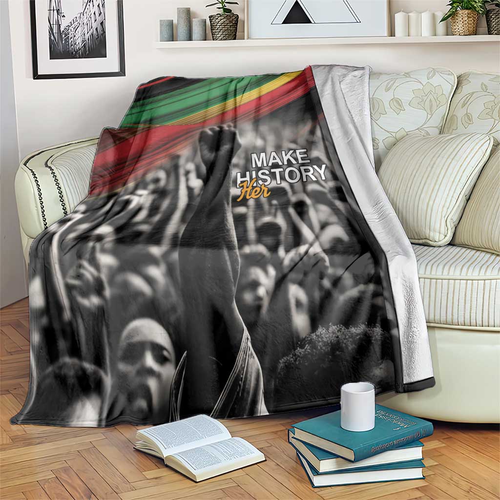 Black-and-white crowd blanket with green-yellow-red stripe top and “MAKE HISTORY Her” print