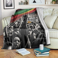 Black-and-white crowd blanket with green-yellow-red stripe top and “MAKE HISTORY Her” print