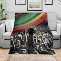 Black crowd photo blanket with green-yellow-red stripe band and “MAKE HISTORY Her” logo