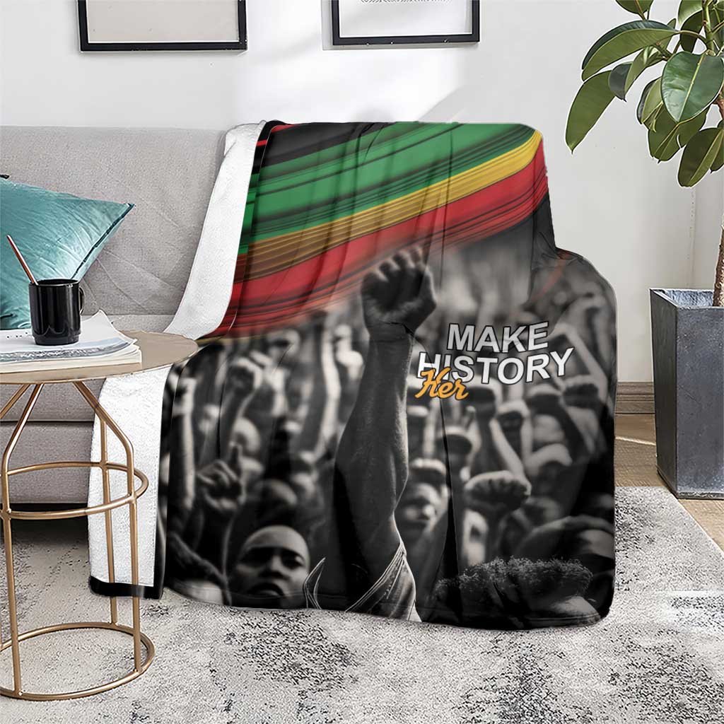 Black-and-white crowd blanket with green, yellow, and red stripe border and “MAKE HISTORY Her”