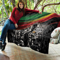 Black quilt held on couch with Pan-African diagonal stripe and 'MAKE HISTORY Her' print