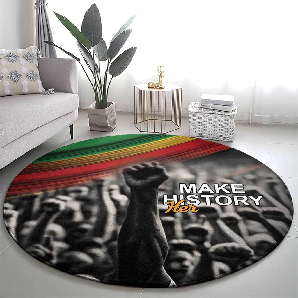 Round black carpet with Make Her text over crowd graphic, green and red stripe band