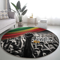 Round black carpet with Make Her text over crowd graphic, green and red stripe band