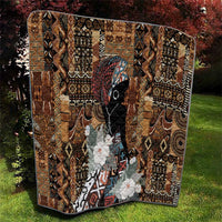 Brown patterned quilt with tribal motifs, black face figure, white flower clusters, dark trim