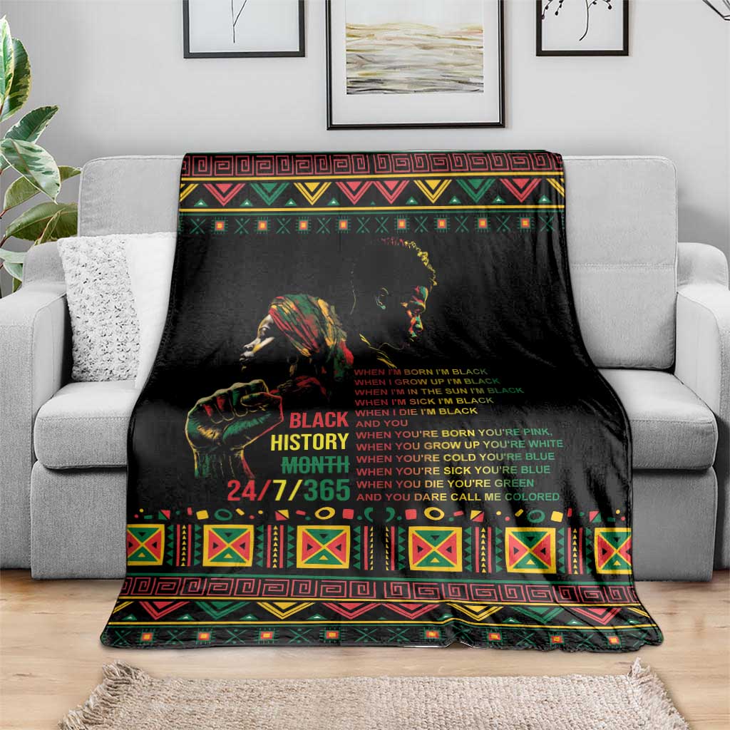 Black history blanket with colorful patterned border and bold text, spread on gray sofa