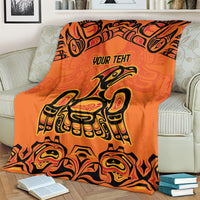 Orange throw blanket with 'YOUR TEXT' and Haida bird and face motifs around edges