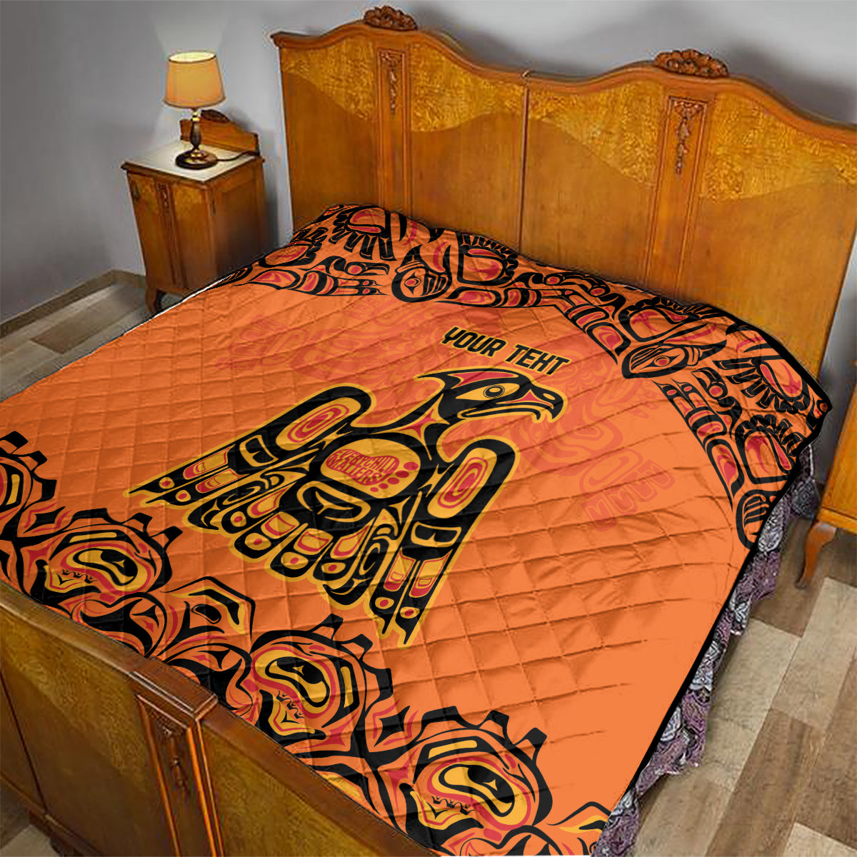 Orange quilt blanket on bed with black border, Haida-style raven and "YOUR TENT" text