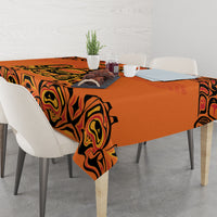 Orange tablecloth with black tribal swirl design, overhanging corners on dining table