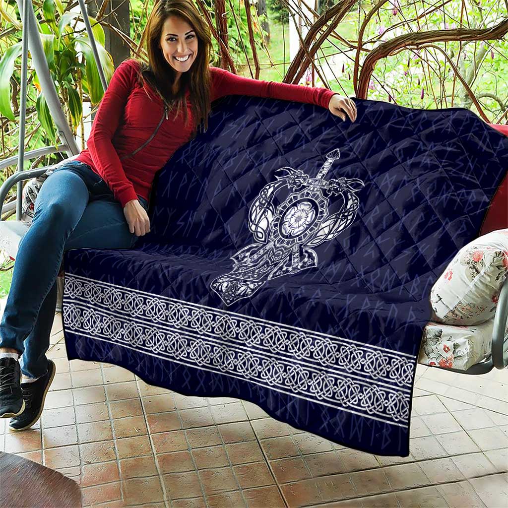 Blue quilt laid over couch with central white Viking axe emblem and decorative border