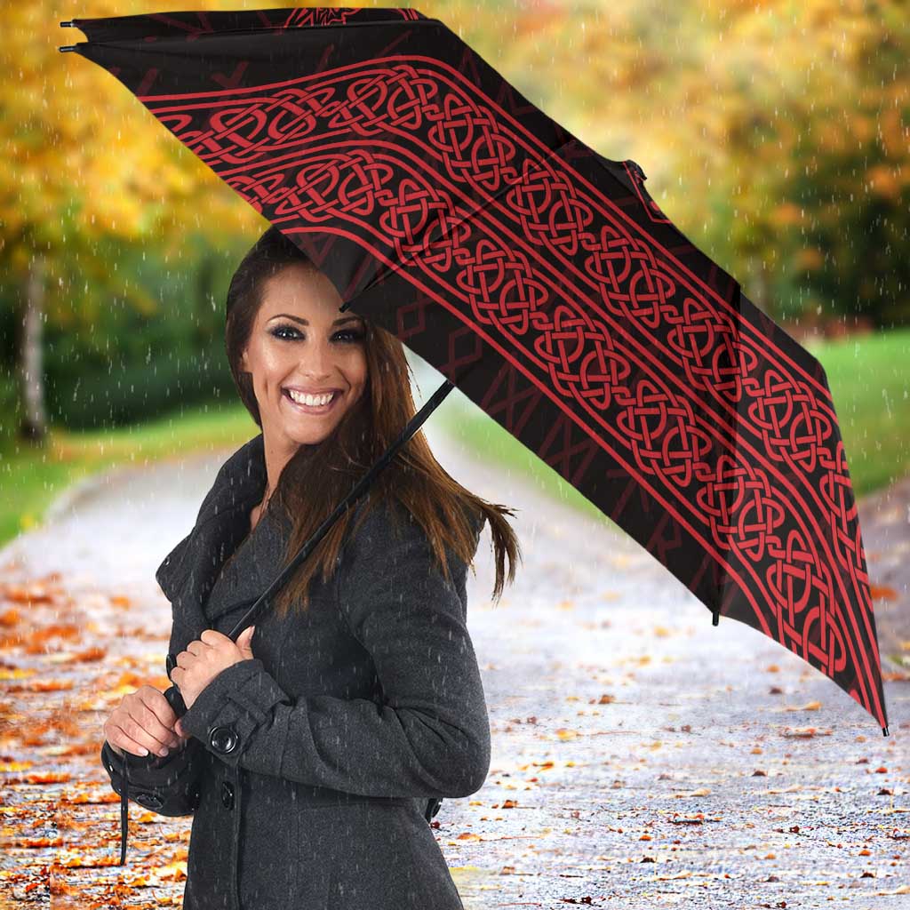 Red-and-black Viking-style umbrella with knotwork print, open above a person