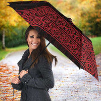 Red-and-black Viking-style umbrella with knotwork print, open above a person