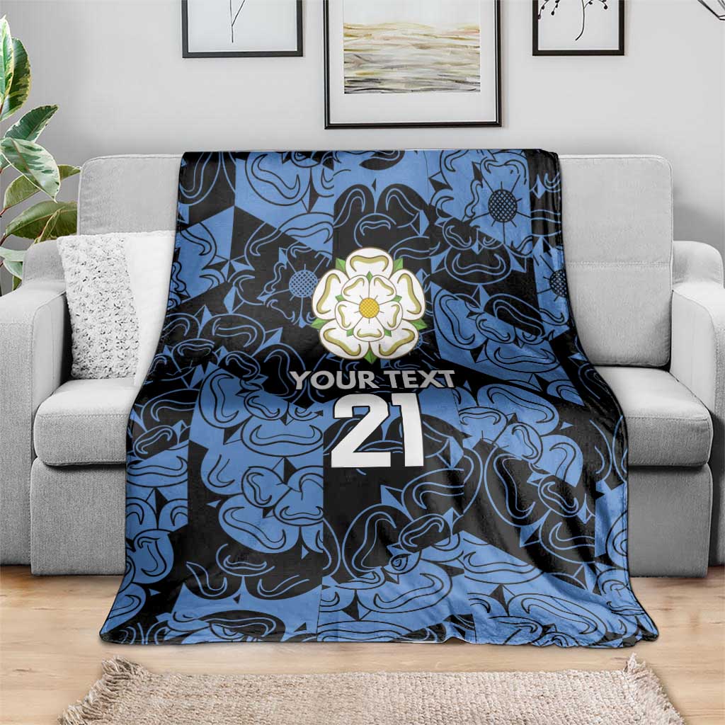 Personalized fleece blanket in blue and navy with flower emblem, 'YOUR TEXT' and 21, spread on sofa