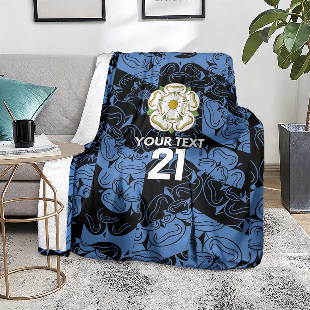 Personalized fleece blanket in blue and navy with flower emblem, 'YOUR TEXT' and 21, draped on sofa
