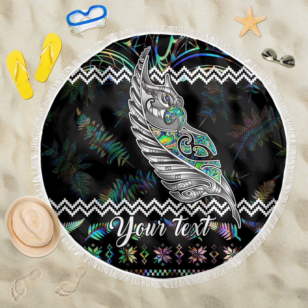 Round black beach blanket with fringed edge, manaia and fern pattern, “Your Text”.