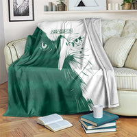 Green and white falcon pattern blanket draped on a sofa with books nearby