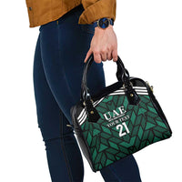Small green and black shoulder handbag with UAE logo and 21 on patterned front.