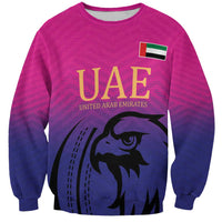 Pink cricket sweatshirt with UAE text, flag, and falcon graphic on front.