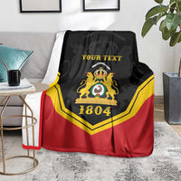 Black/red/yellow personalized throw blanket with crest and “YOUR TEXT”, 1804 on floor