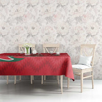 Red tablecloth on dining table with green motif; set styled with chairs.