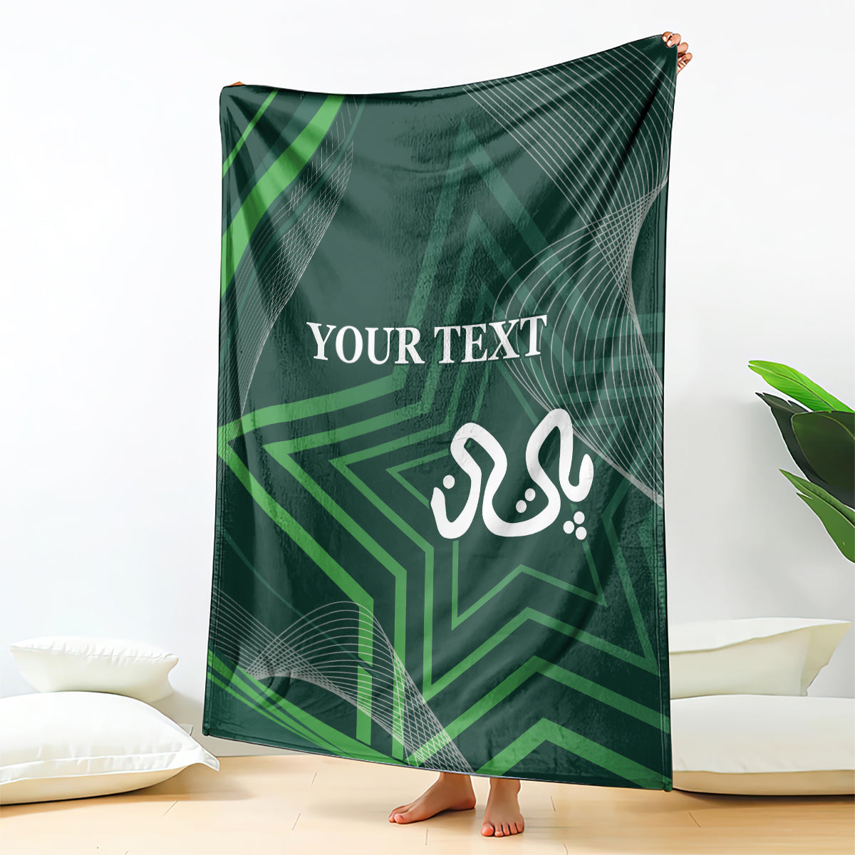 Green throw blanket held up indoors, featuring “YOUR TEXT” and calligraphy-style emblem