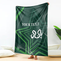 Green throw blanket held up indoors, featuring “YOUR TEXT” and calligraphy-style emblem