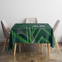 Green geometric tablecloth covering dining table with four chairs around it