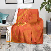 Orange blanket with gold custom text and wave design, spread over a gray couch seat