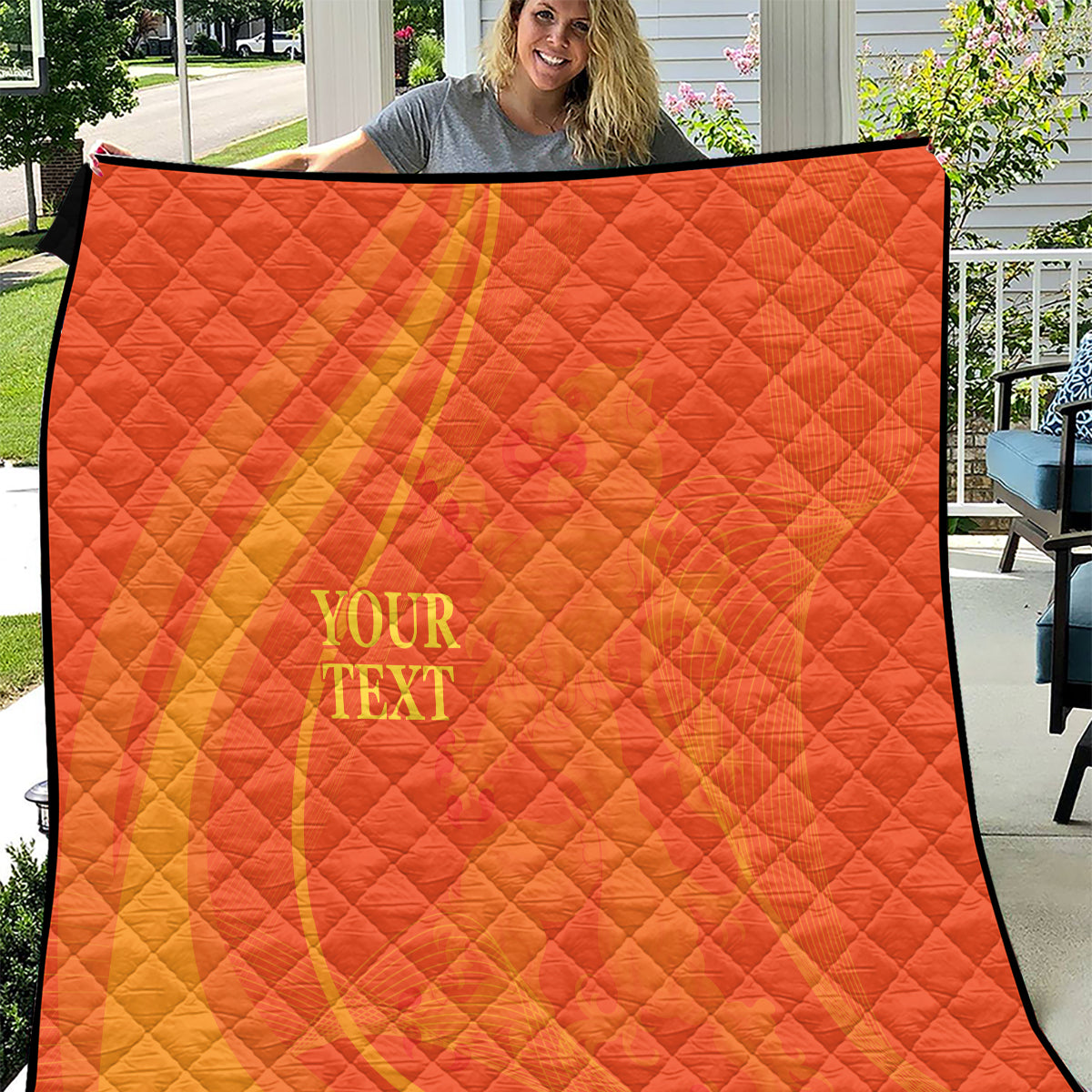 Orange quilt blanket with yellow diagonal stripe, diamond quilting, and “YOUR TEXT” on front.