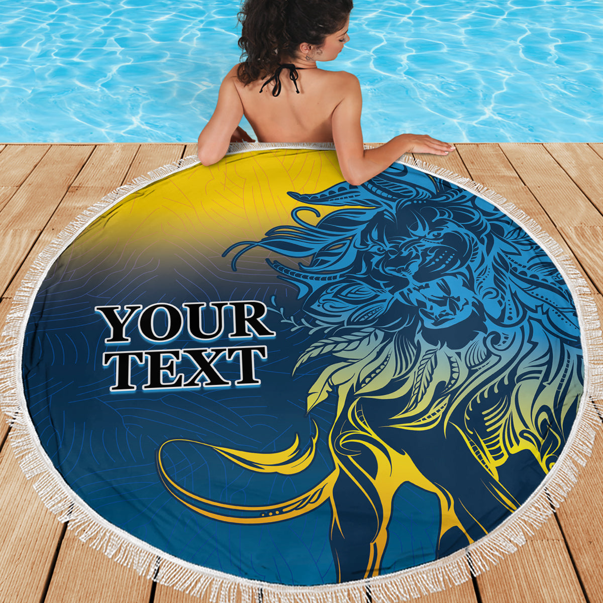 Round beach blanket with blue-and-yellow lion design and white fringed border on deck