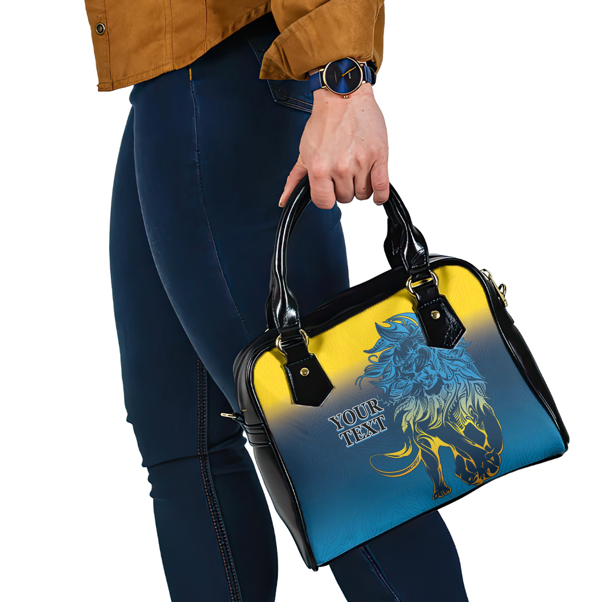 Blue and yellow lion print handbag with black handles, held at the side by hand.