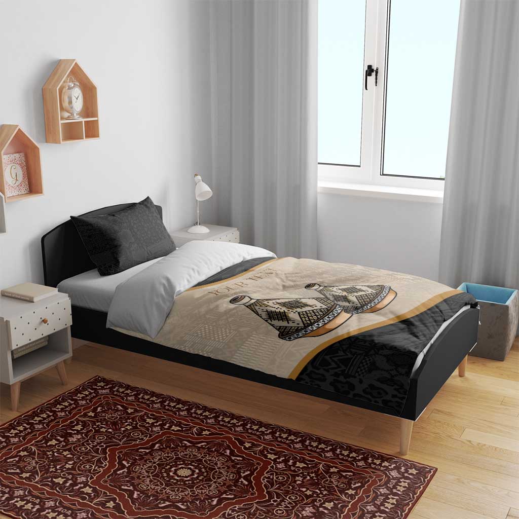Bedding set on bed: beige-and-black duvet with tribal artwork and gold stripe, two pillows.