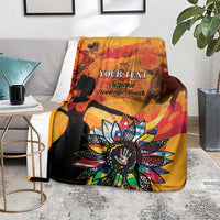 Personalized throw blanket draped over seating, gold-orange and black with “Your Text”