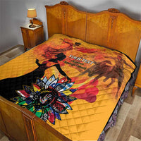 Gold quilt on bed with red dancer silhouettes and colorful flower emblem, quilted stitching.