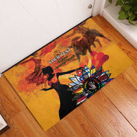 Personalized rubber doormat on wood floor, gold with black silhouettes and bright flower emblem