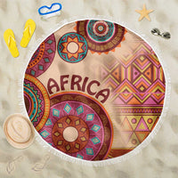 Beige round beach blanket with multicolor African tribal design and white tassel fringe.