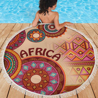Round beige African tribal beach blanket with colorful mandala motif and white fringe edge.