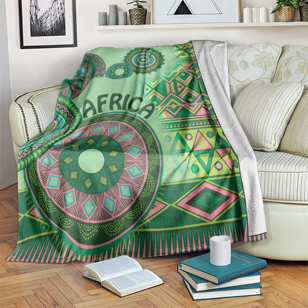 Green tribal pattern blanket on a sofa with mandala medallion and pink-trimmed zigzags