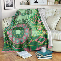 Green tribal pattern blanket on a sofa with mandala medallion and pink-trimmed zigzags