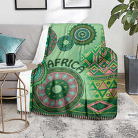 Green tribal pattern blanket folded on a chair, featuring central circular mandala