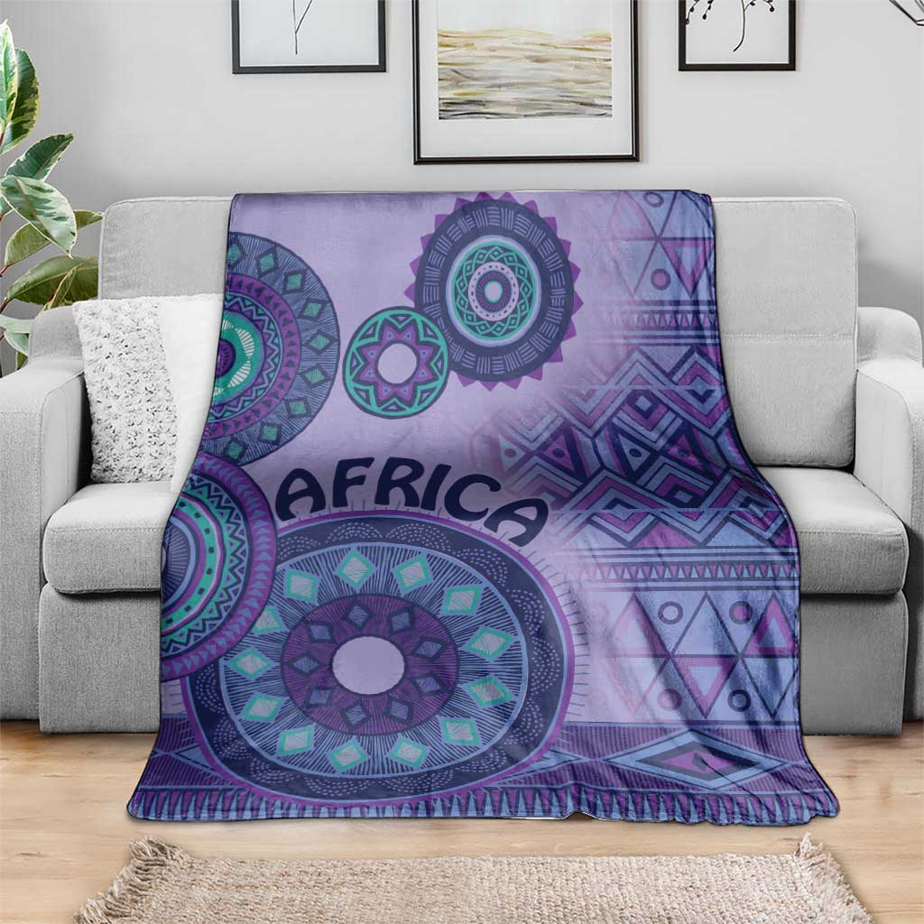 Purple tribal geometric blanket draped over gray couch, fringed bottom and medallions