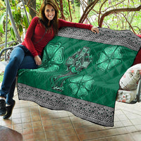 Green quilt displayed on a couch with Celtic cross, harp, shamrock motifs and patterned black border.