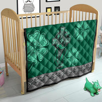 Green quilt on crib with Celtic cross, harp and shamrock designs and black-and-white decorative trim.