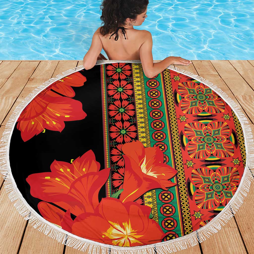 Round beach blanket with black base, red-orange flower print and white fringed edge