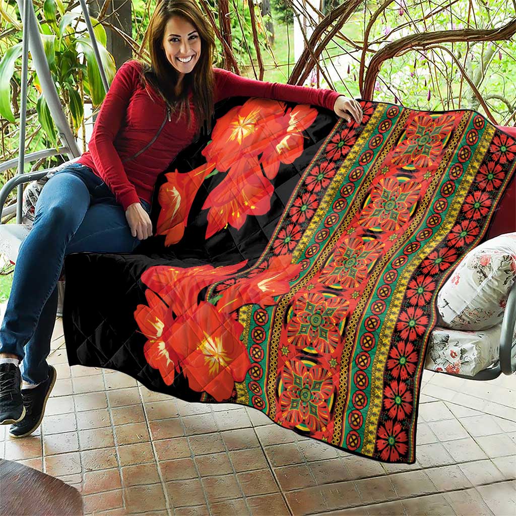 Black quilt with red-orange flowers and green-yellow patterned stripes, laid across couch