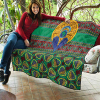 Green traditional kanga-style quilt held up, showing central blue figure with yellow circular halo
