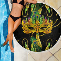 Round fringe beach blanket over poolside tile: black gold mask with green feather motifs